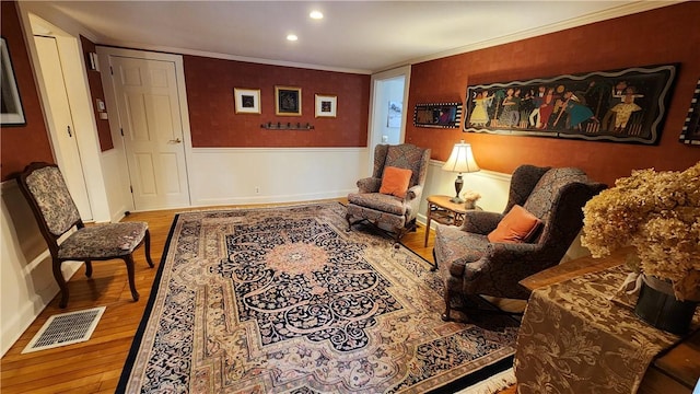 living area with a wainscoted wall, visible vents, recessed lighting, ornamental molding, and wood-type flooring