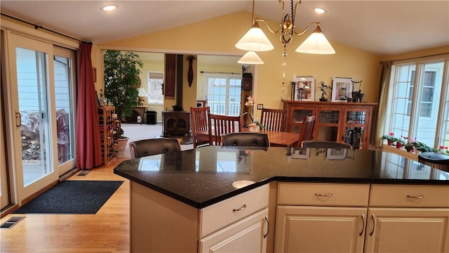 kitchen with light wood-type flooring, visible vents, pendant lighting, a wood stove, and vaulted ceiling