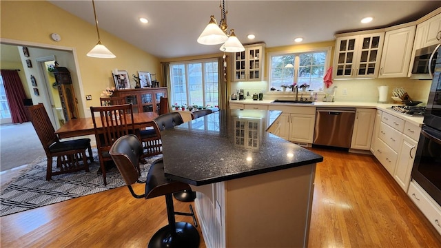 kitchen featuring a breakfast bar, a sink, stainless steel appliances, light wood-style floors, and vaulted ceiling