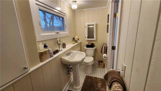 half bath with tile patterned floors, toilet, crown molding, and a sink