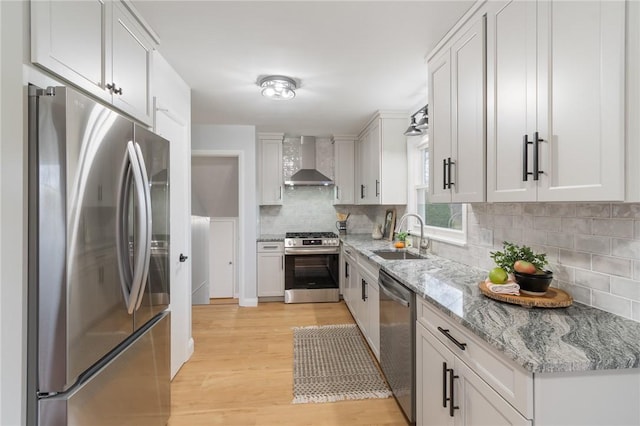 kitchen featuring light wood-type flooring, a sink, backsplash, stainless steel appliances, and wall chimney range hood