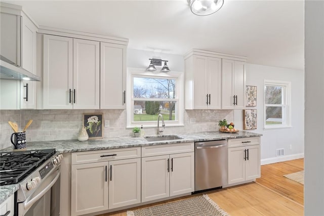 kitchen with light stone counters, light wood-style flooring, appliances with stainless steel finishes, white cabinets, and a sink