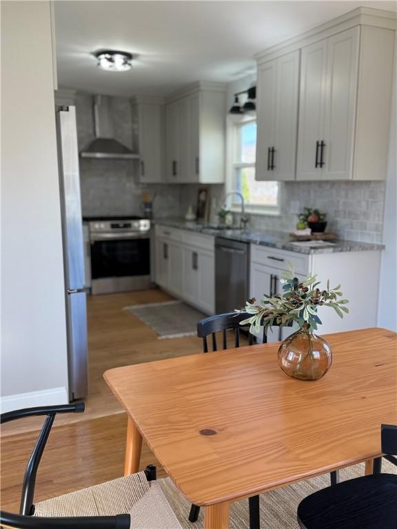 kitchen featuring oven, a sink, freestanding refrigerator, wall chimney range hood, and dishwashing machine