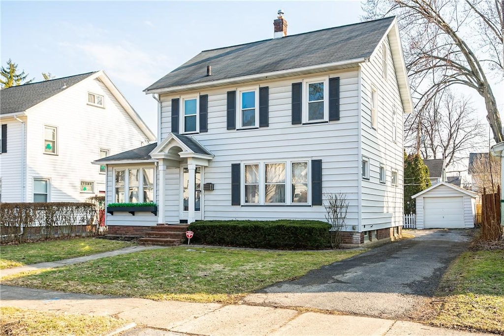 view of front facade featuring an outbuilding, a chimney, a front lawn, a garage, and aphalt driveway