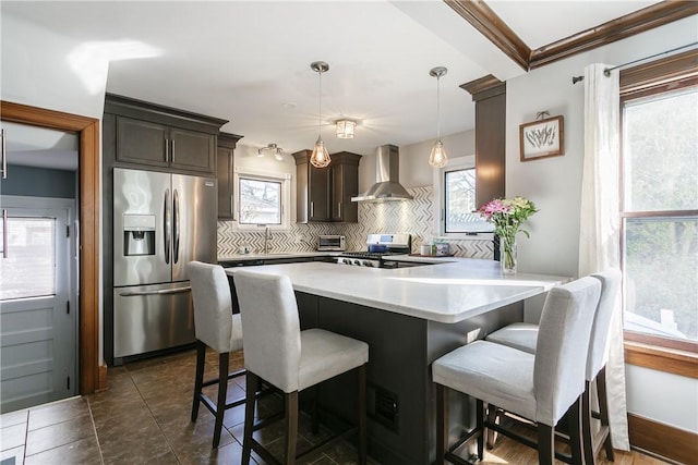 kitchen featuring a breakfast bar, tasteful backsplash, stainless steel appliances, wall chimney exhaust hood, and light countertops