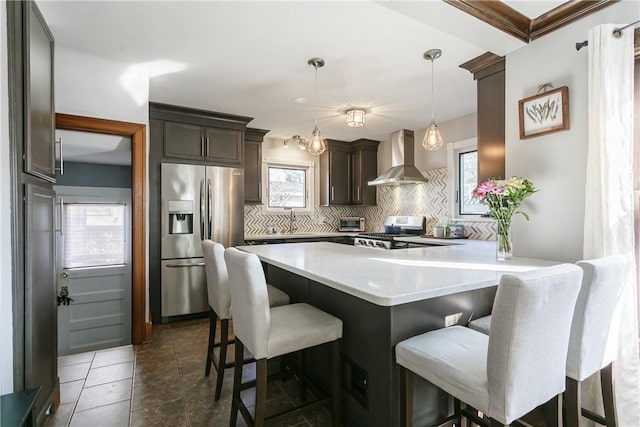 kitchen featuring dark brown cabinets, wall chimney range hood, decorative backsplash, a peninsula, and stainless steel appliances