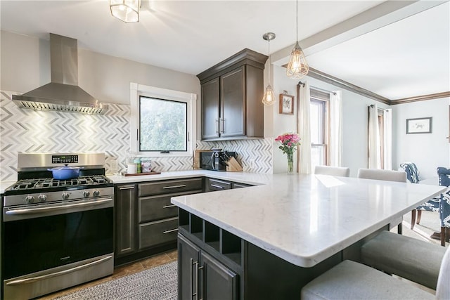 kitchen featuring wall chimney range hood, gas range, a breakfast bar area, a peninsula, and plenty of natural light