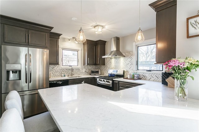 kitchen with a sink, stainless steel appliances, wall chimney range hood, light stone countertops, and dark brown cabinets