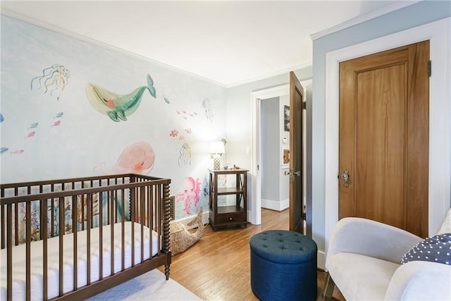 bedroom featuring a crib, baseboards, light wood finished floors, and ornamental molding