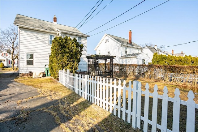 view of property exterior featuring a fenced front yard, a chimney, and a pergola