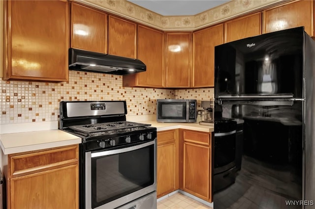 kitchen featuring under cabinet range hood, stainless steel appliances, backsplash, and light countertops