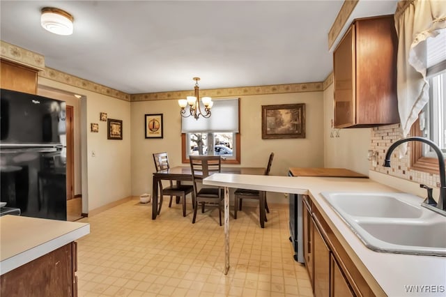 kitchen featuring light countertops, freestanding refrigerator, an inviting chandelier, and a sink