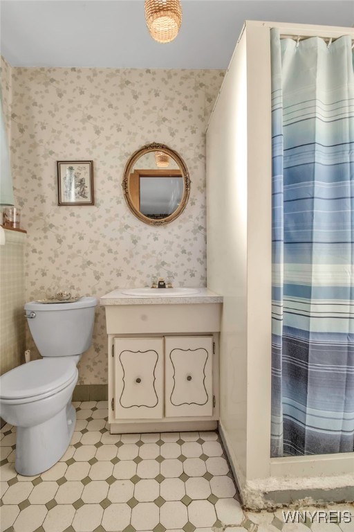 bathroom with baseboards, toilet, vanity, and wallpapered walls