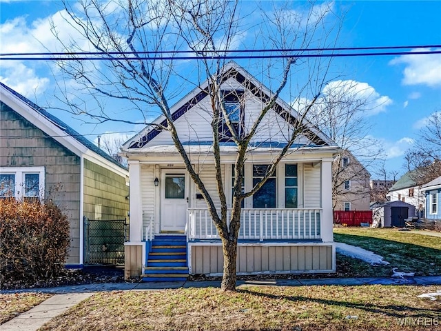 bungalow-style house with a porch, an outdoor structure, a front yard, and fence