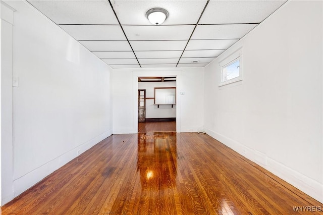 empty room featuring wood finished floors, a paneled ceiling, and baseboards