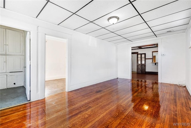 spare room featuring a drop ceiling, baseboards, and wood finished floors