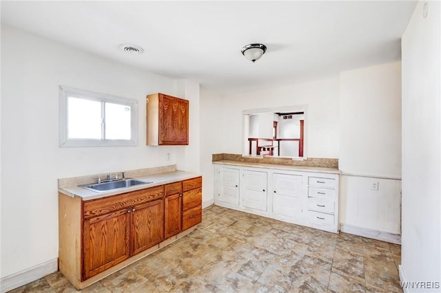 kitchen featuring brown cabinetry, baseboards, visible vents, a sink, and light countertops