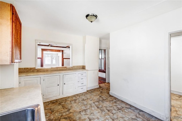 kitchen with stone finish flooring, light countertops, baseboards, and a sink