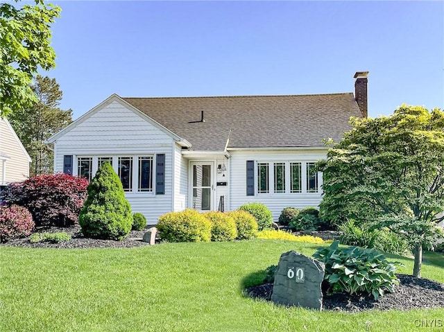 view of front of house featuring a chimney, roof with shingles, and a front lawn