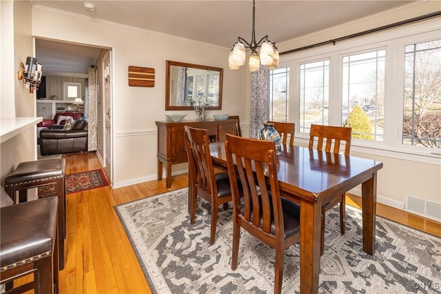 dining space with baseboards, visible vents, an inviting chandelier, ornamental molding, and light wood-style floors