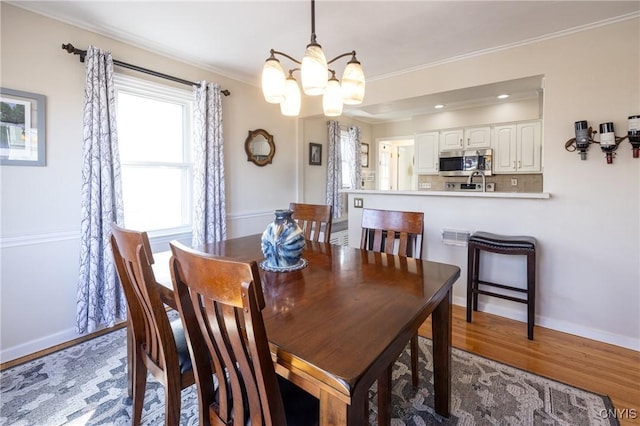 dining area with a notable chandelier, ornamental molding, baseboards, and wood finished floors