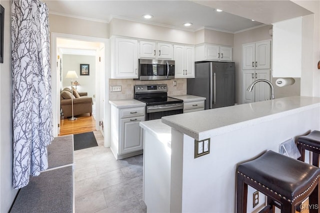 kitchen with a breakfast bar, light countertops, appliances with stainless steel finishes, white cabinetry, and backsplash