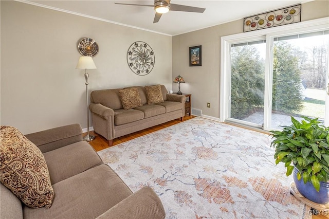 living area with visible vents, crown molding, ceiling fan, baseboards, and wood finished floors