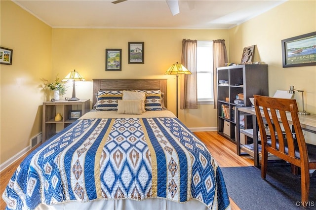 bedroom featuring baseboards, wood finished floors, visible vents, and ornamental molding