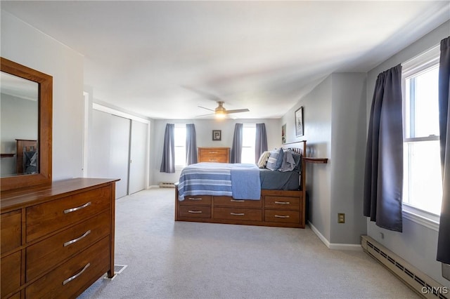 bedroom with a baseboard heating unit, light carpet, a closet, and a ceiling fan