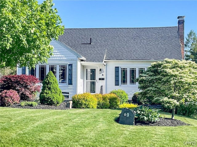 cape cod-style house with a chimney, a shingled roof, and a front lawn