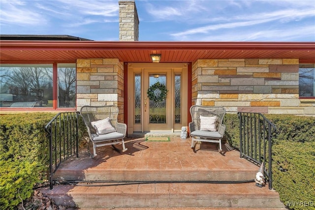 entrance to property featuring stone siding, a porch, and a chimney