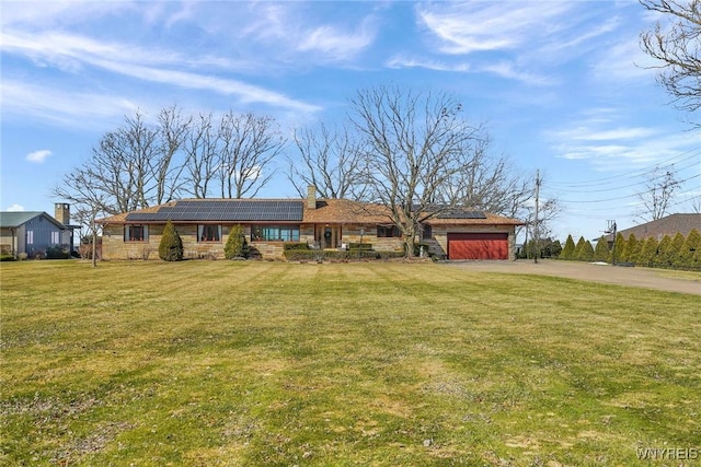 ranch-style home with solar panels, concrete driveway, a garage, and a front lawn