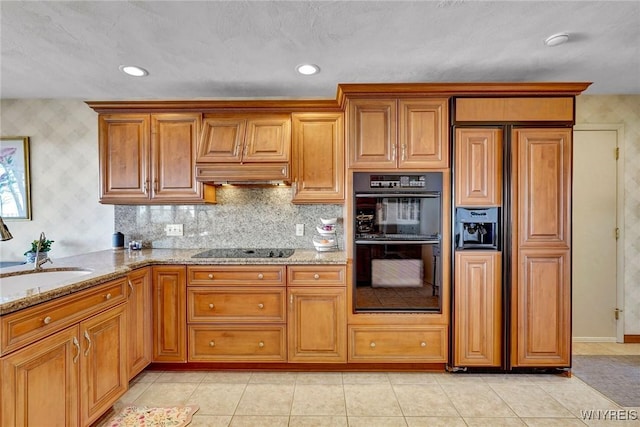 kitchen featuring black appliances, light stone countertops, brown cabinets, and a sink