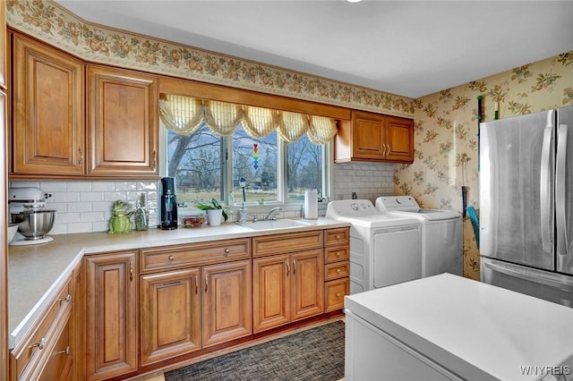 clothes washing area featuring wallpapered walls, separate washer and dryer, and a sink