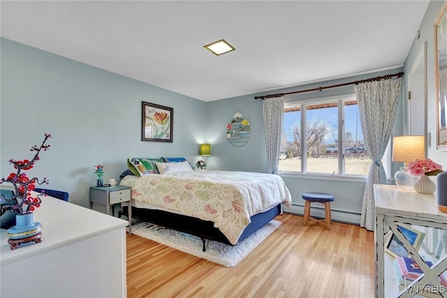 bedroom with a baseboard heating unit and light wood-style flooring