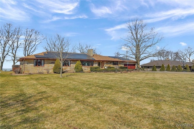 back of property with solar panels, a chimney, and a yard