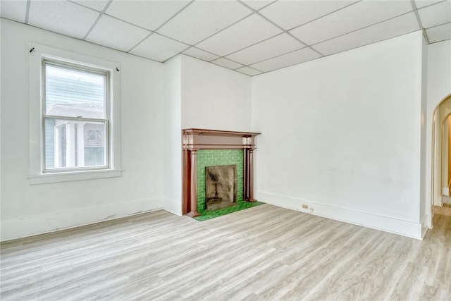 unfurnished living room with a drop ceiling, arched walkways, wood finished floors, and a tile fireplace