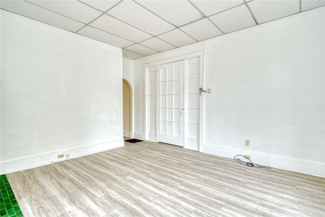 unfurnished room featuring wood finished floors, a paneled ceiling, arched walkways, and baseboards