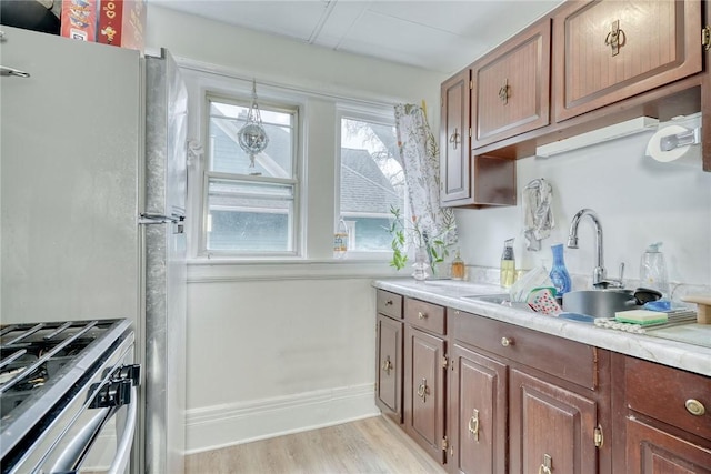 kitchen with light wood-type flooring, a sink, stainless steel appliances, light countertops, and baseboards