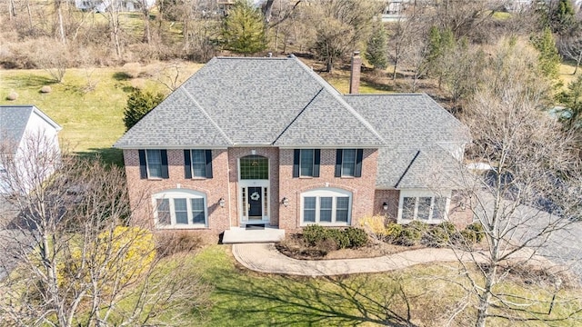 view of front facade with brick siding, a shingled roof, and a front yard