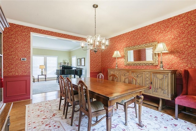 dining area featuring light wood-style flooring, wallpapered walls, crown molding, wainscoting, and a chandelier