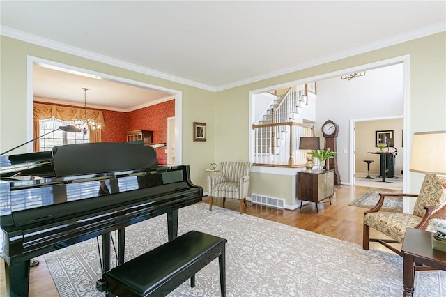 living area featuring visible vents, ornamental molding, wood finished floors, an inviting chandelier, and baseboards