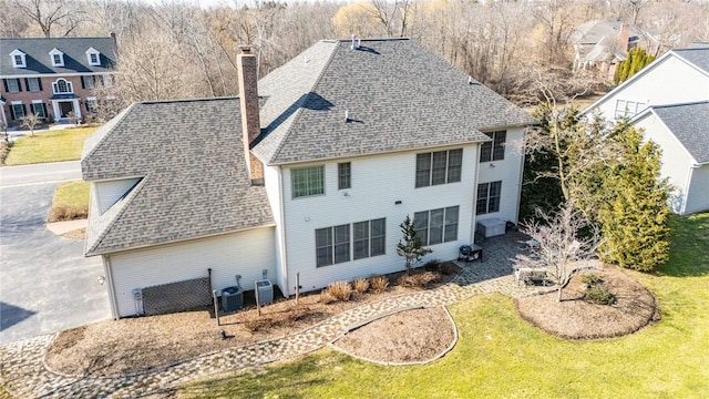 back of property with central air condition unit, a chimney, a yard, and a shingled roof