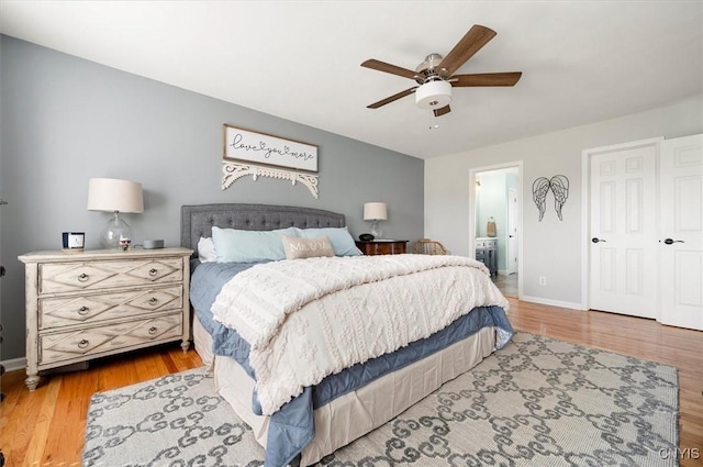 bedroom with ceiling fan, connected bathroom, baseboards, and wood finished floors