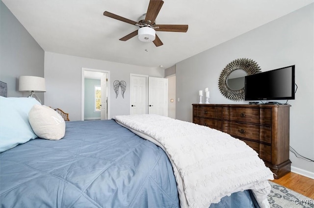 bedroom featuring a ceiling fan, ensuite bath, wood finished floors, and baseboards