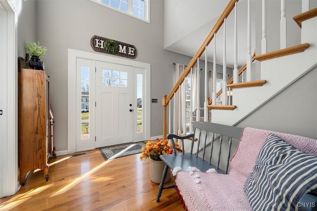 foyer featuring visible vents, wood finished floors, stairway, a high ceiling, and baseboards