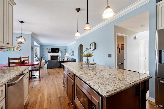 kitchen with a center island, light stone countertops, a tiled fireplace, appliances with stainless steel finishes, and light wood-style floors