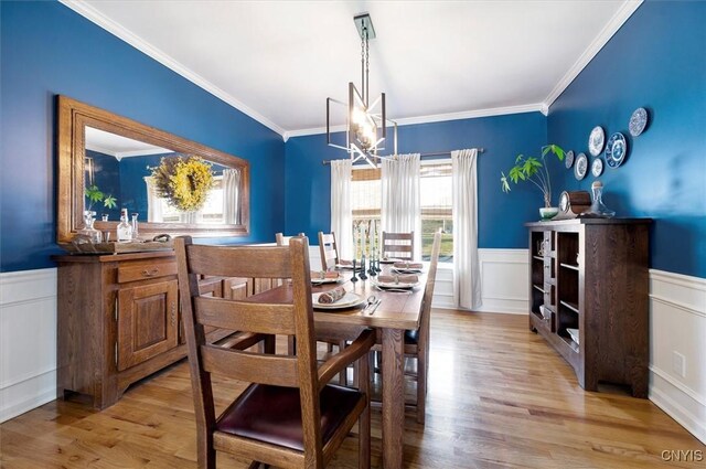 dining area featuring a chandelier, a wainscoted wall, light wood-style flooring, and crown molding