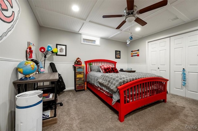 carpeted bedroom with a closet, visible vents, a ceiling fan, and a wainscoted wall