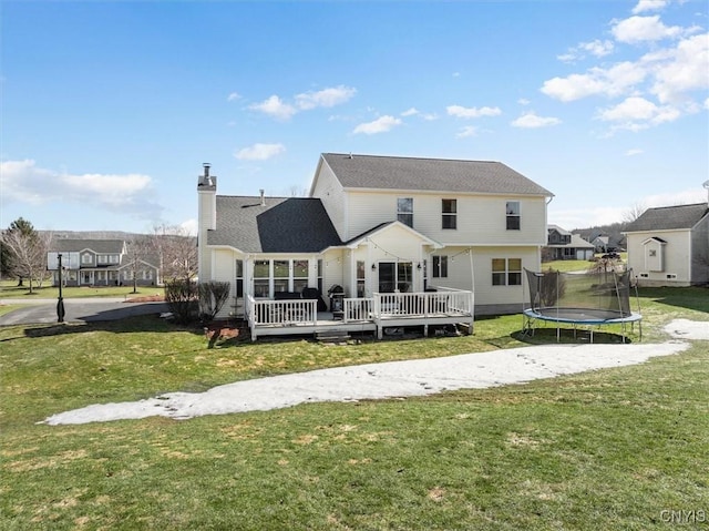 rear view of property with a chimney, a lawn, a wooden deck, and a trampoline